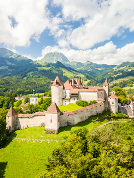 Gruyères Castle surrounded by lush green hills and mountains in Switzerland.