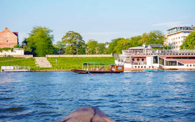 Boat on Vistula River during Cracow city tour, with riverside view and greenery.