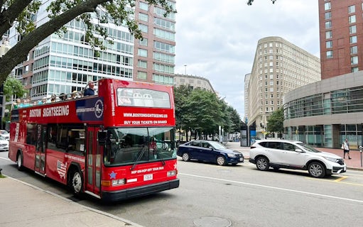 Open-top Boston sightseeing bus on city street with modern buildings.
