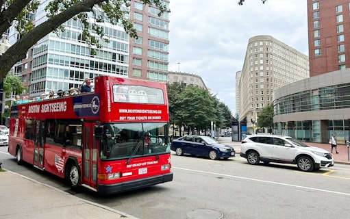 Open-top Boston sightseeing bus on city street with modern buildings.