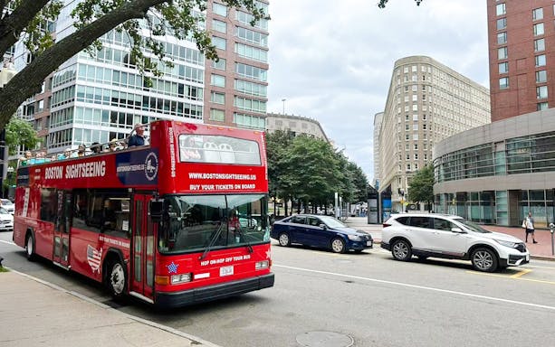 Open-top Boston sightseeing bus on city street with modern buildings.