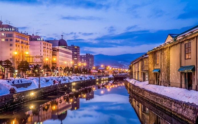Otaru Canal in Hokkaido during winter evening with snow-covered banks and illuminated buildings.