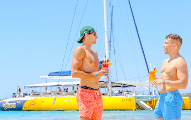 Men holding juice glasses beside a yellow catamaran, South Sea Sailing, Fiji.