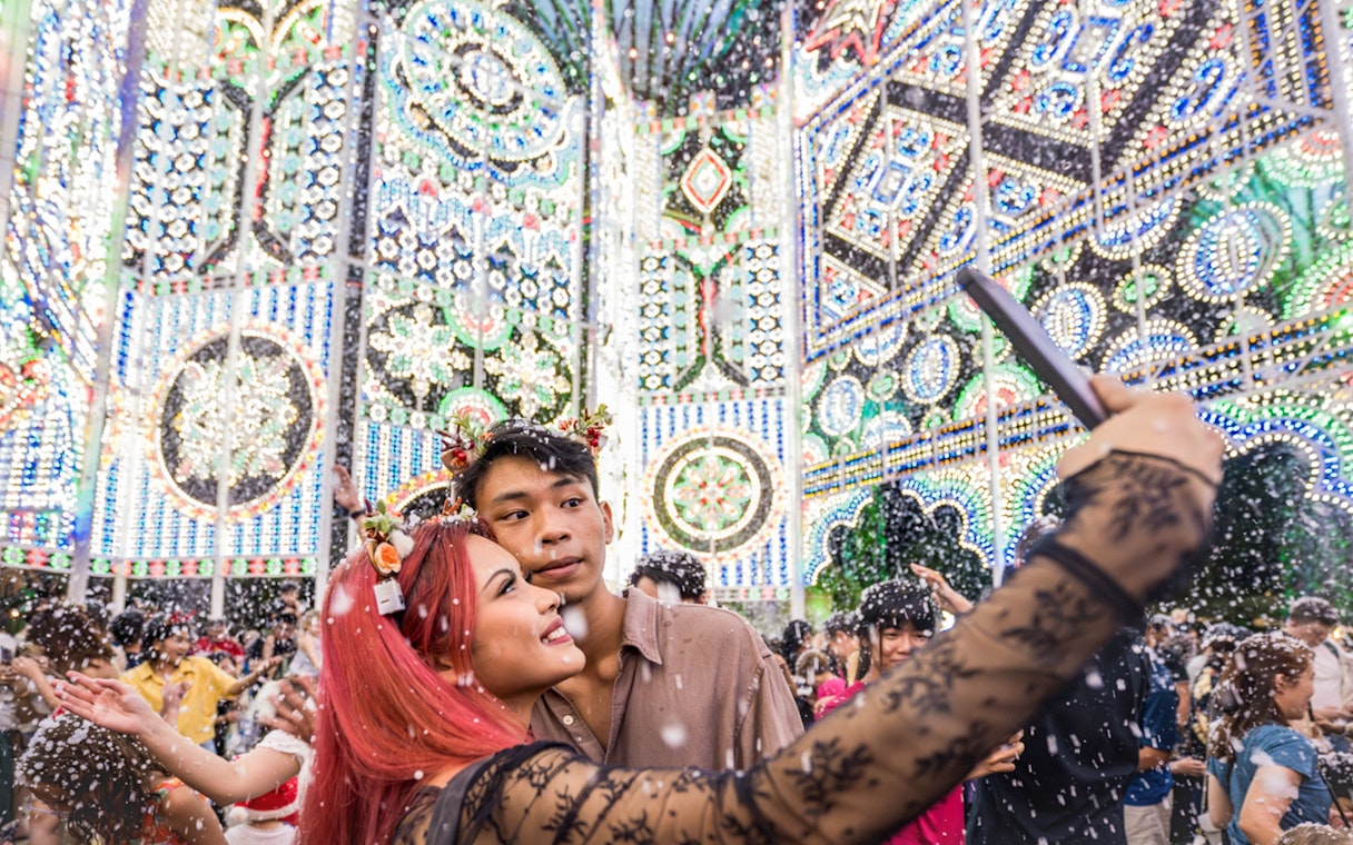 Couple taking selfie at Christmas Wonderland, GBB Cloud Forest with festive lights and snow.