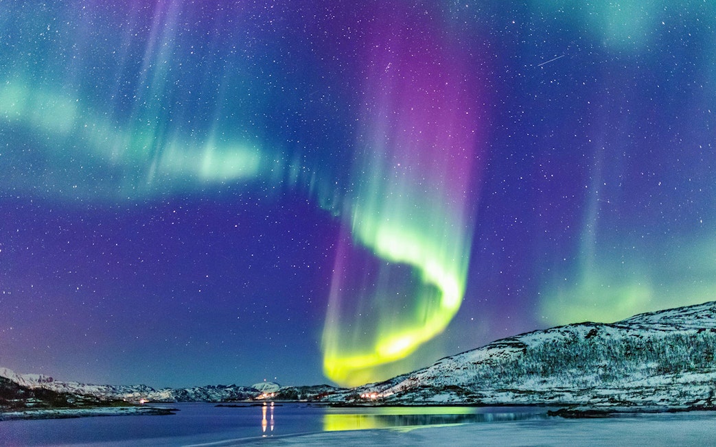 Northern Lights over snowy mountains and water in Tromso, Norway.