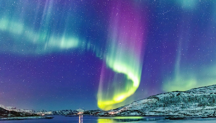 Northern Lights over snowy mountains and water in Tromso, Norway.