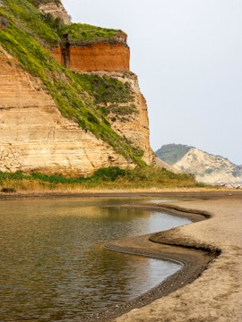 Rocky coastline with layered cliffs and water at Campi Flegrei, Italy.