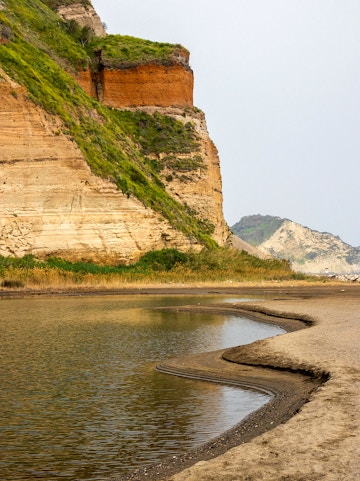 Rocky coastline with layered cliffs and water at Campi Flegrei, Italy.