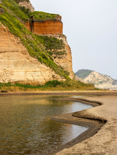 Rocky coastline with layered cliffs and water at Campi Flegrei, Italy.