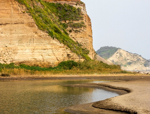 Rocky coastline with layered cliffs and water at Campi Flegrei, Italy.