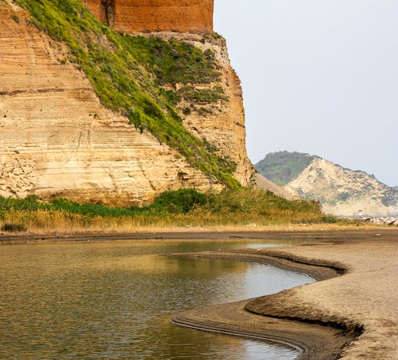 Rocky coastline with layered cliffs and water at Campi Flegrei, Italy.