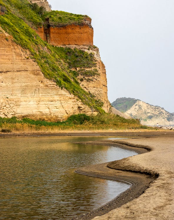 Rocky coastline with layered cliffs and water at Campi Flegrei, Italy.