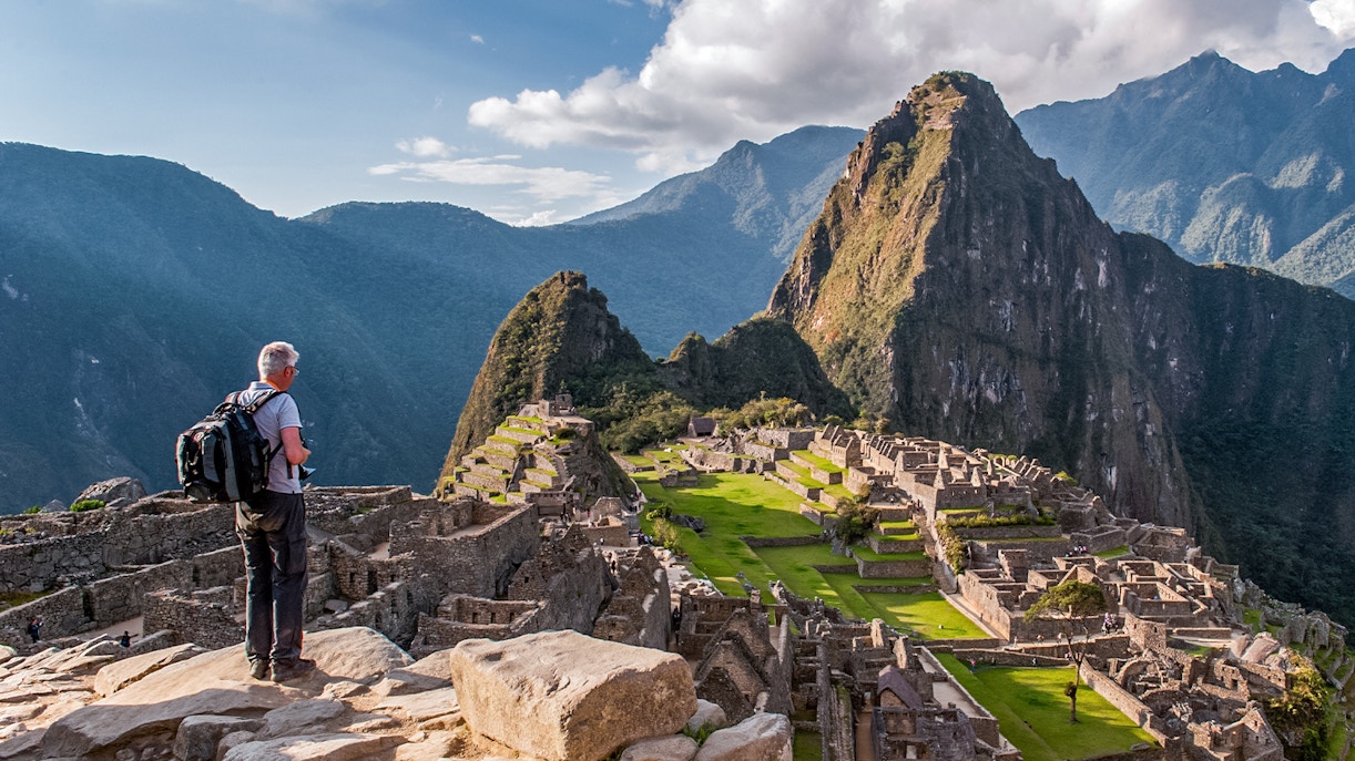 Traveler overlooking Machu Picchu ruins with Huayna Picchu in the background, Peru.