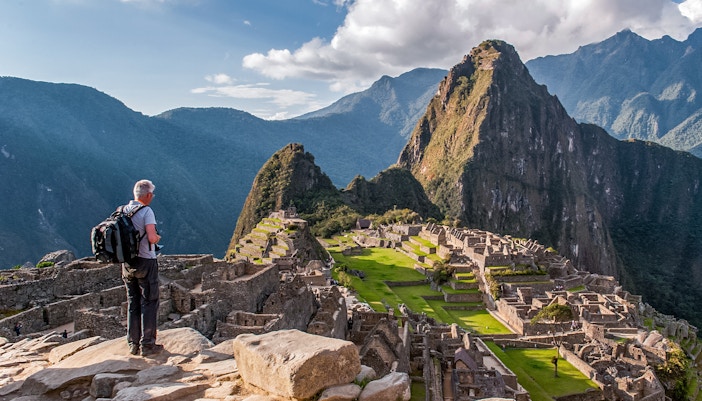 Traveler overlooking Machu Picchu ruins with Huayna Picchu in the background, Peru.
