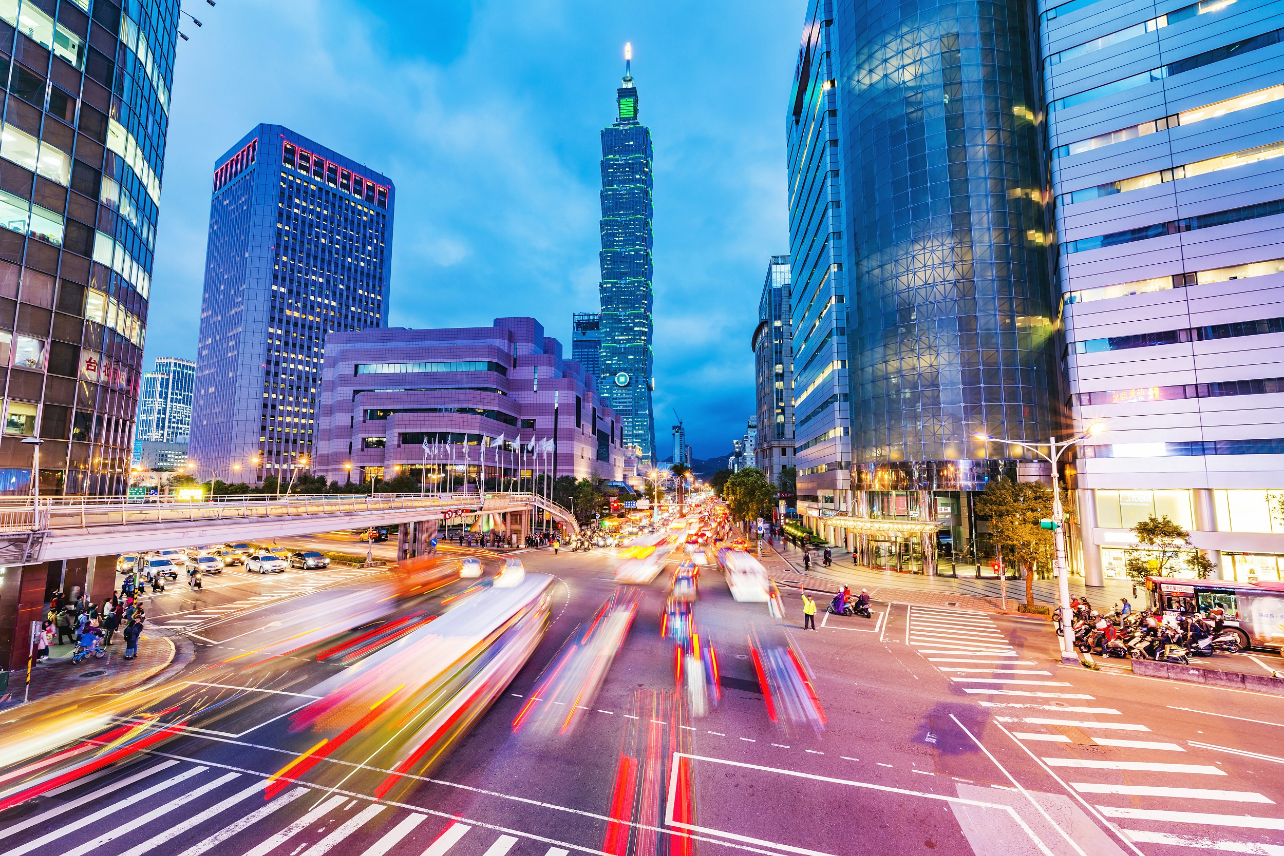 Taipei 101 illuminated at night with busy city traffic in the foreground.