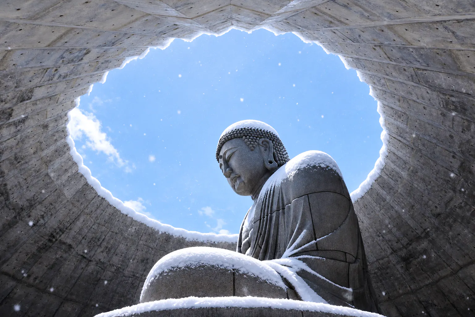 Buddha statue covered in snow at Atama Daibutsu, Hokkaido, under a circular opening.