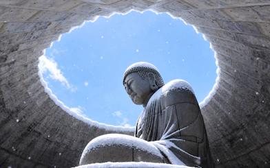 Buddha statue covered in snow at Atama Daibutsu, Hokkaido, under a circular opening.