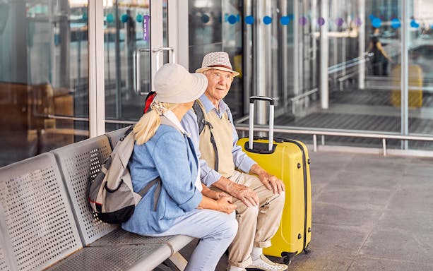 Elderly couple with luggage waiting at Mallorca Airport entrance for private transfer.
