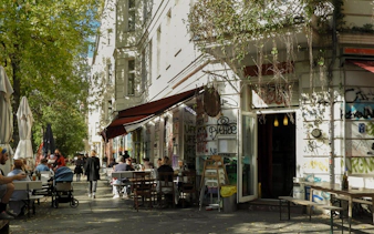 Outdoor cafe scene in Kreuzberg with people dining along a graffiti-covered street.