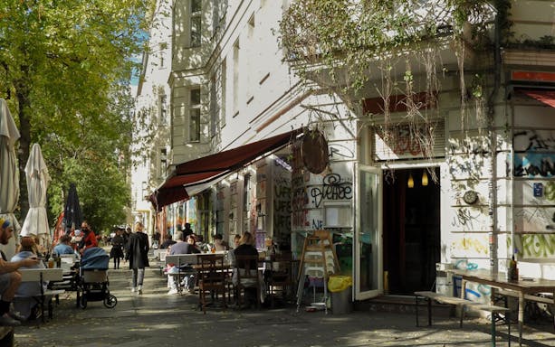 Outdoor cafe scene in Kreuzberg with people dining along a graffiti-covered street.