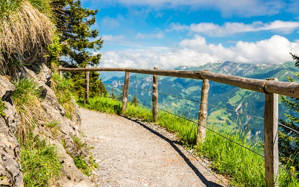 Pathway with wooden railing on Mount Stanserhorn, offering scenic views of Swiss Alps.