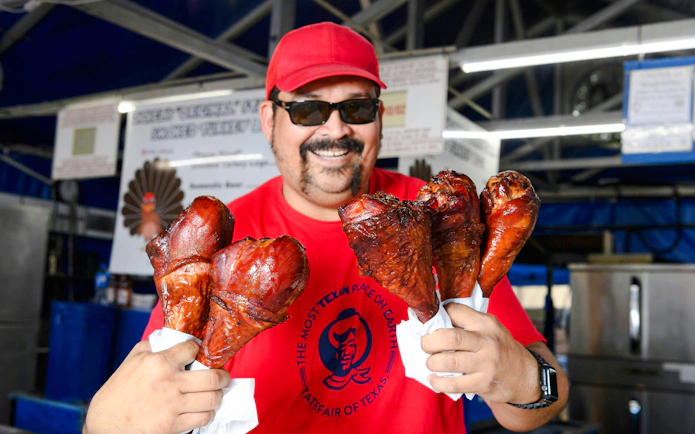 Man holding smoked turkey legs at State Fair of Texas food stall.