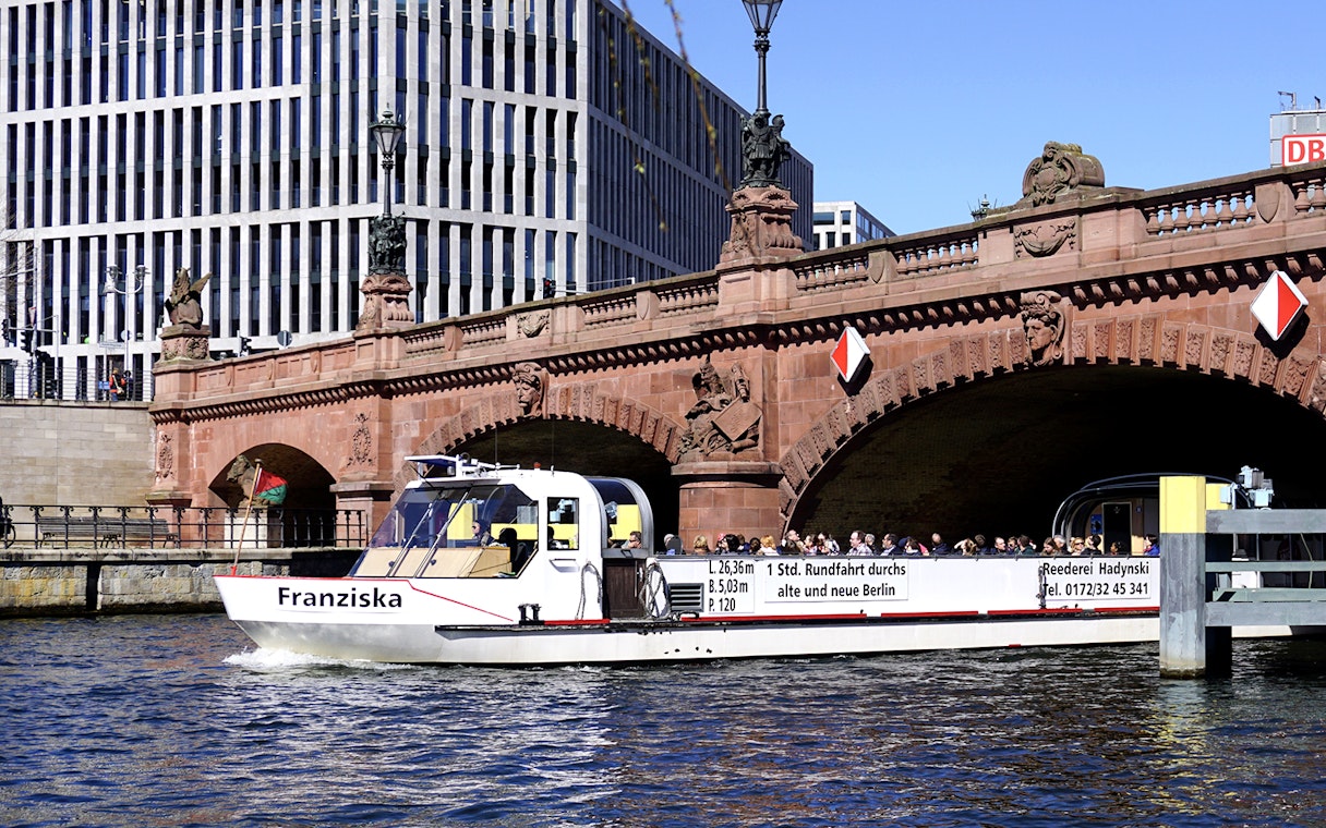 River cruise boat passing under a historic bridge in Berlin with tour guide.