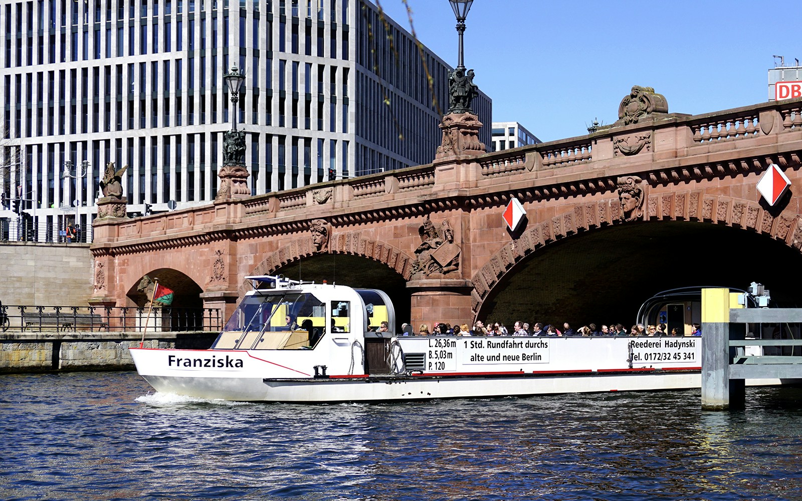 River cruise boat passing under a historic bridge in Berlin with tour guide.