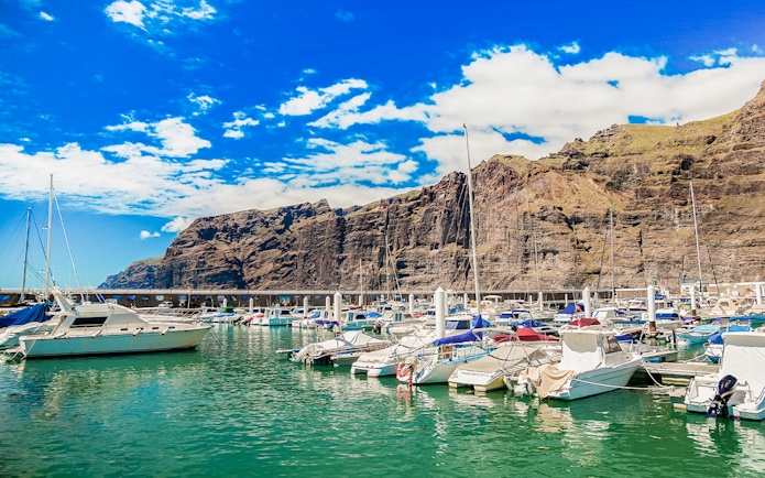 Yachts and boats docked at Los Gigantes marina with cliffs in the background.