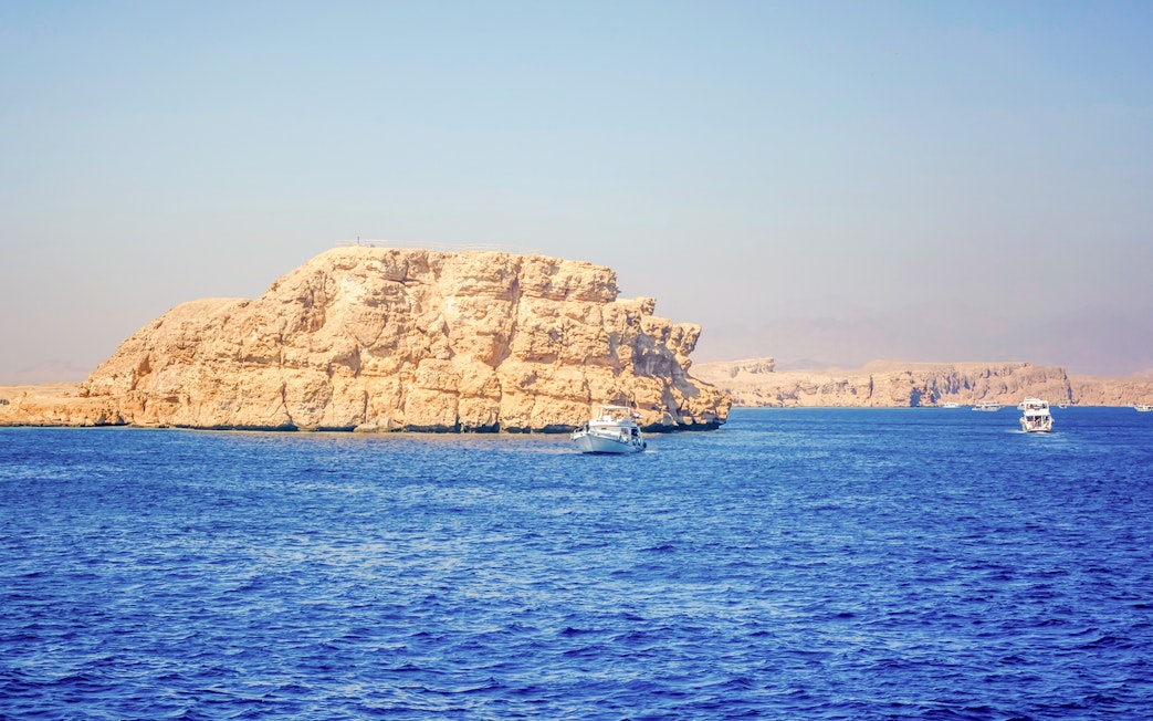 Boats near rocky White Island, Sharm El-Sheikh, surrounded by blue sea.