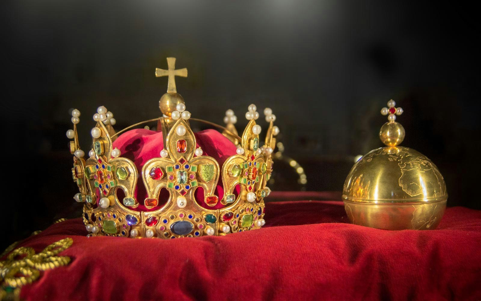 Crown jewels on a red velvet pillow, featuring a gold crown with gemstones and an orb.