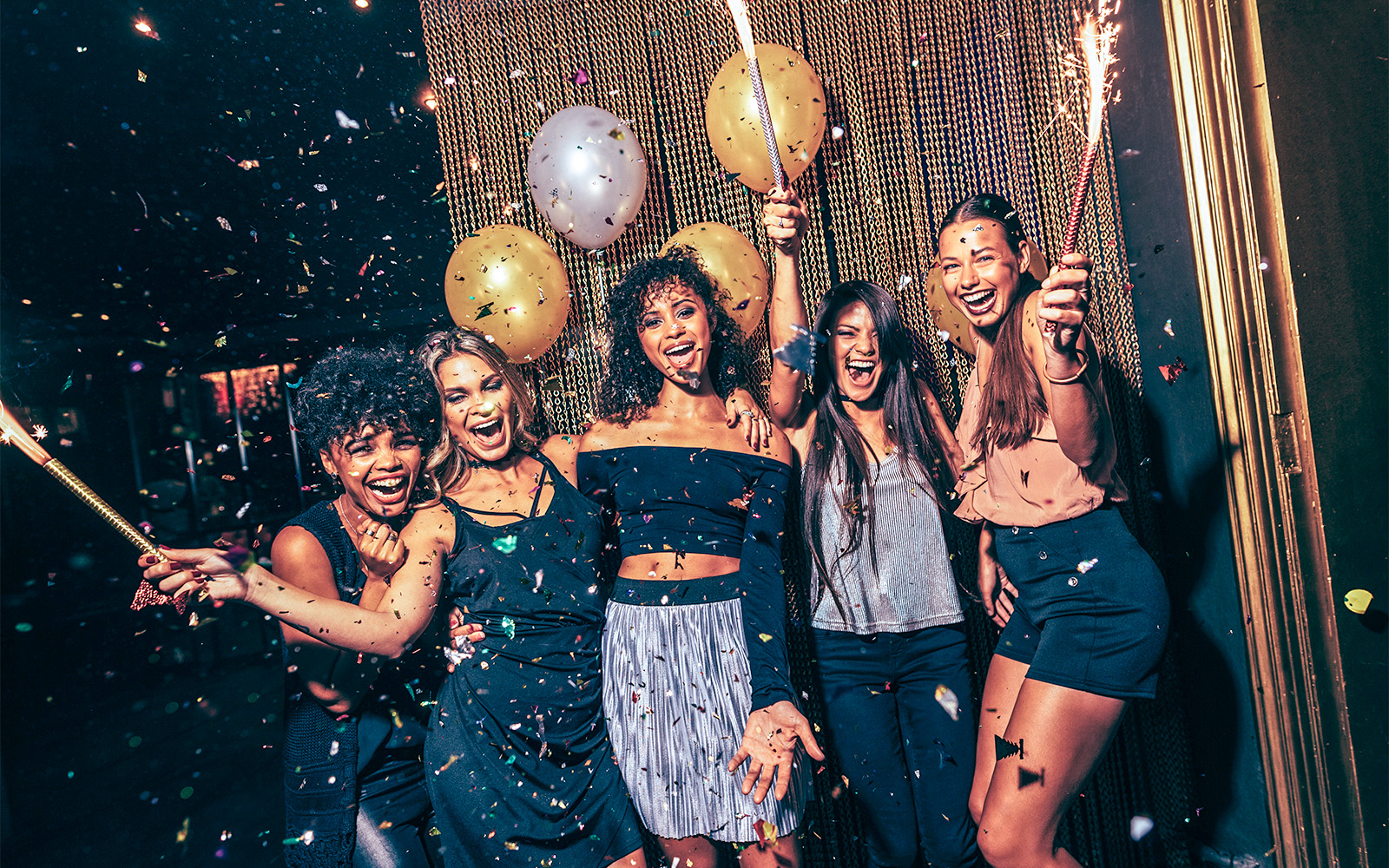 Group celebrating New Year's Eve 2023 in London with sparklers and balloons.