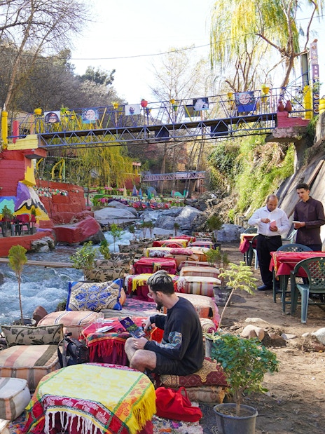 Tourist dining by a river in a colorful restaurant, Ourika Valley, Morocco.