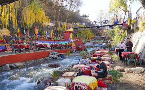 Tourist dining by a river in a colorful restaurant, Ourika Valley, Morocco.