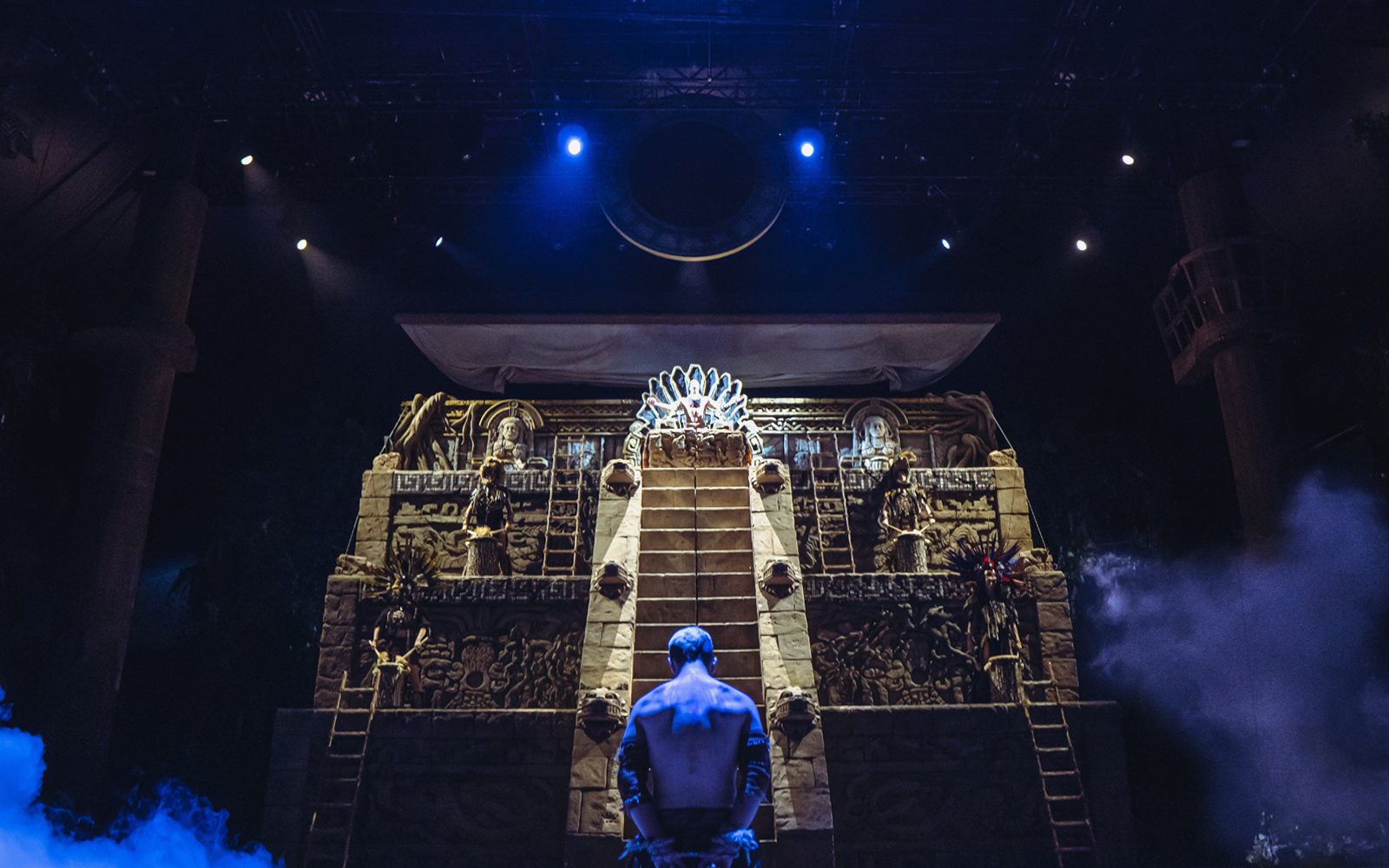 Stage scene from "MALINCHE, un musical de Nacho Cano" with a performer facing an illuminated pyramid.