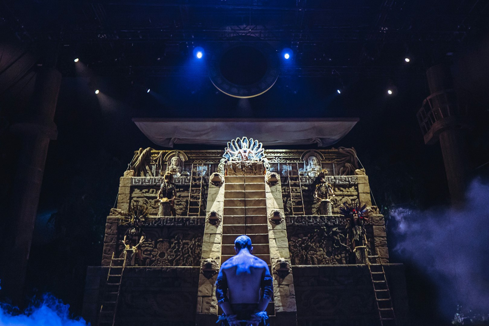 Stage scene from "MALINCHE, un musical de Nacho Cano" with a performer facing an illuminated pyramid.