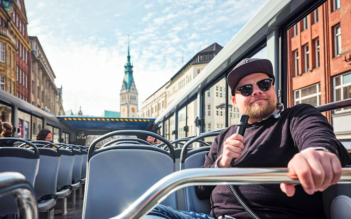 Hop-On Hop-Off bus tour in Hamburg with view of city architecture and guide holding microphone.