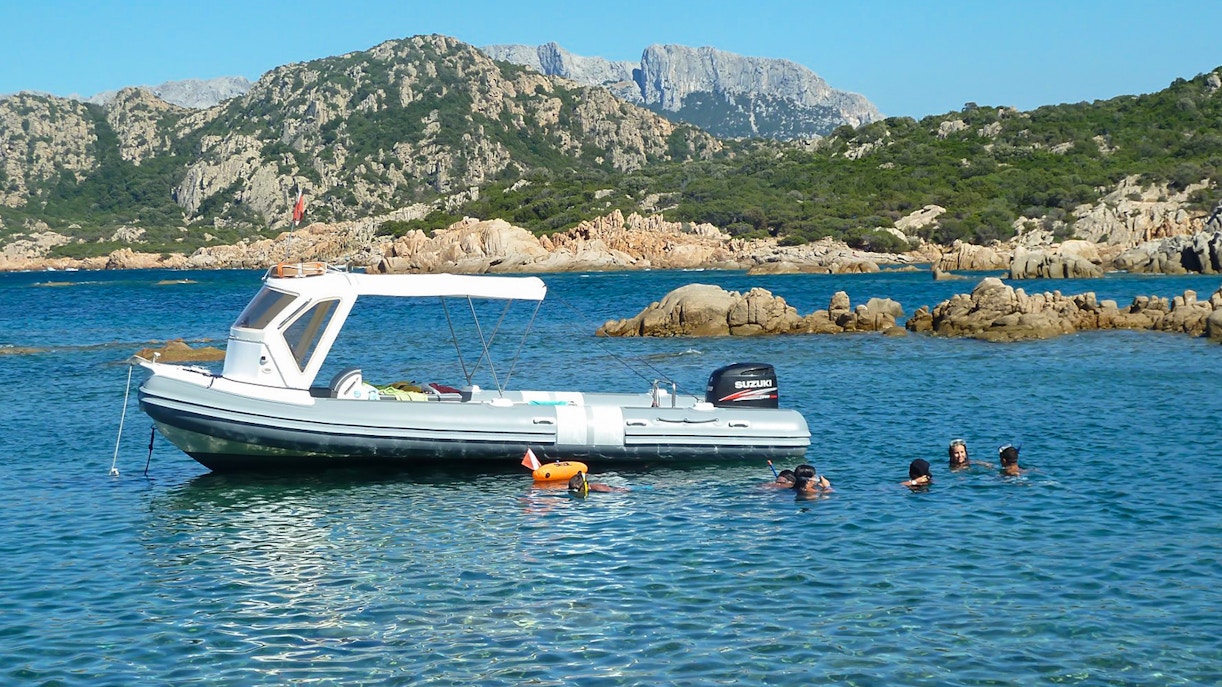 Dinghy with snorkelers near Tavolara Island, Italy, surrounded by rocky landscape.