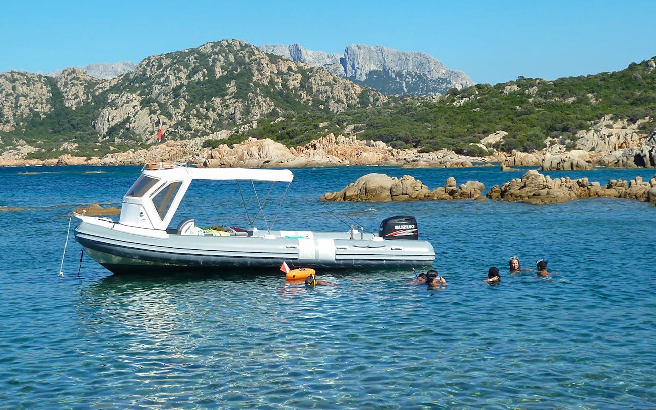 Dinghy with snorkelers near Tavolara Island, Italy, surrounded by rocky landscape.