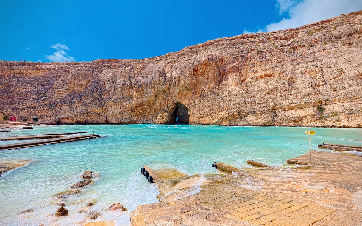 Coastal view of Gozo's Azure Window site with clear blue water and rocky cliffs.