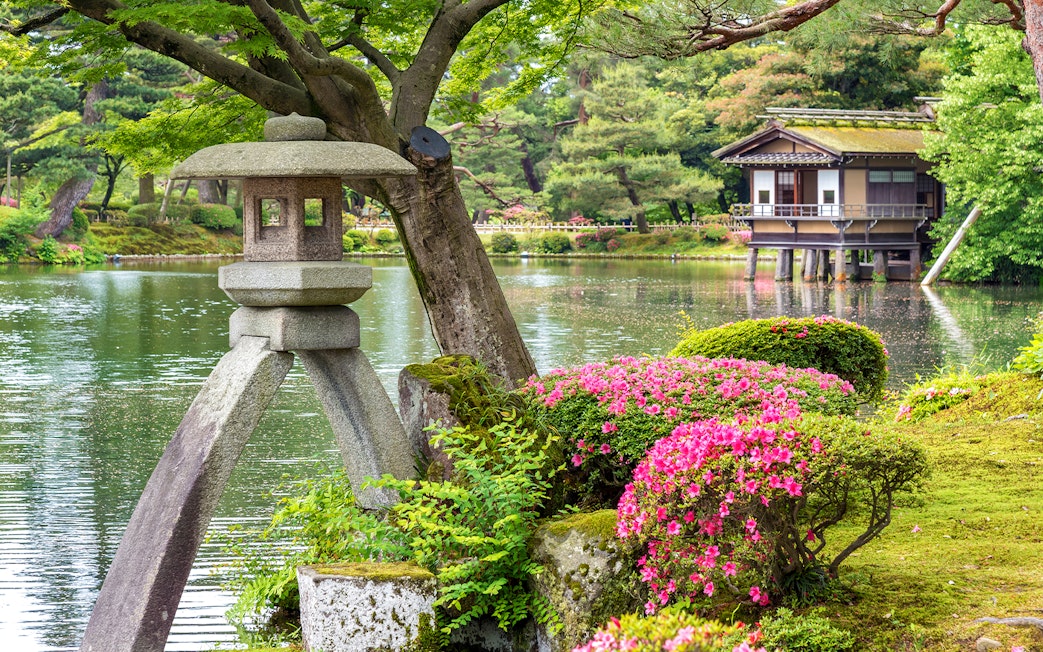 Stone lantern and vibrant azaleas by the pond in Kenrokuen Garden, Kanazawa, Japan.