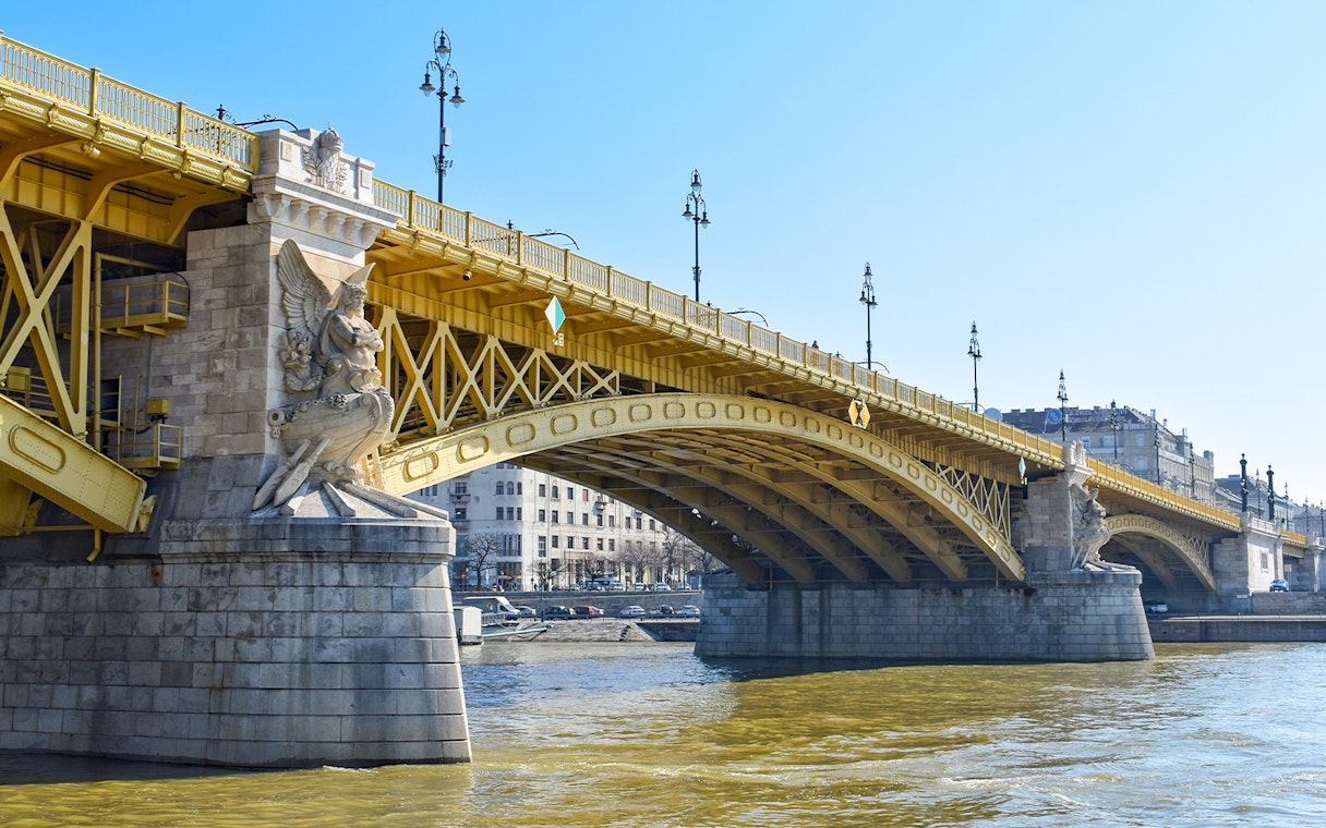 Margaret Bridge in Budapest with ornate stone sculptures and yellow arches over the Danube River.
