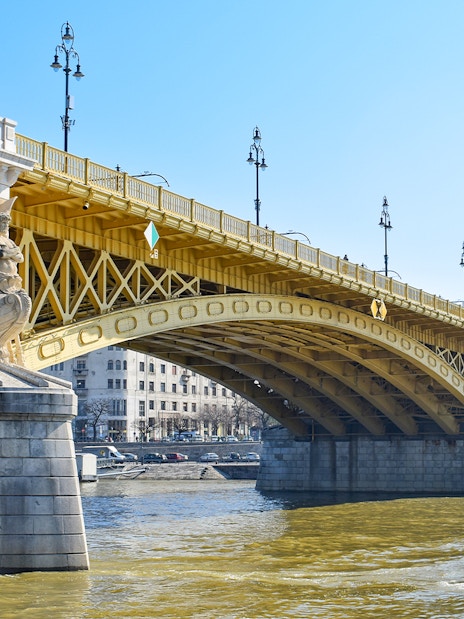 Margaret Bridge in Budapest with ornate stone sculptures and yellow arches over the Danube River.