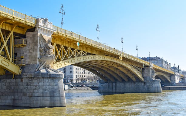 Margaret Bridge in Budapest with ornate stone sculptures and yellow arches over the Danube River.