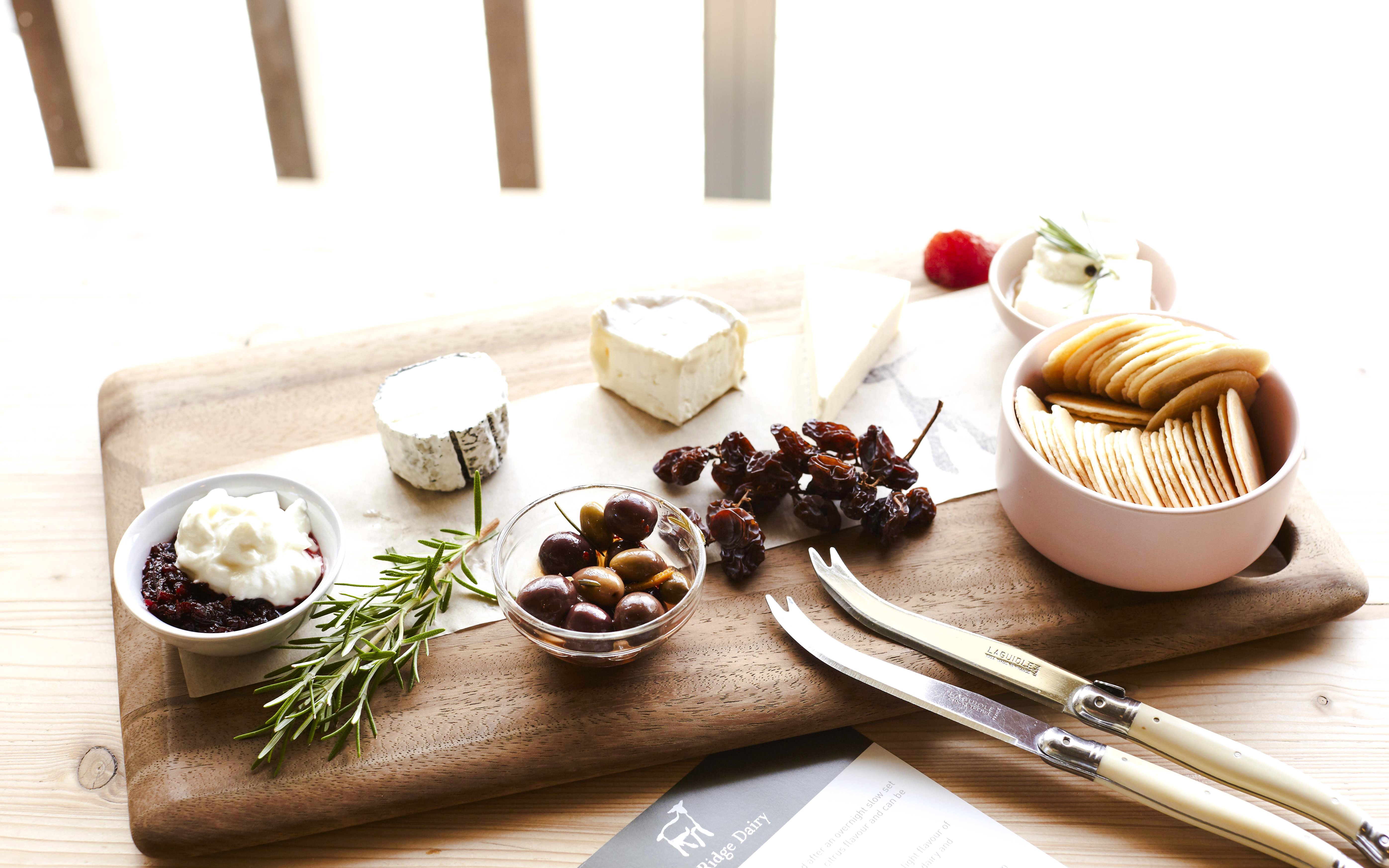 Cheese platter with Yarra Valley cheeses, olives, crackers, and dried fruits on a wooden board.