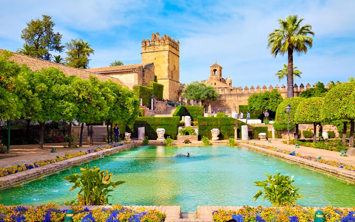Gardens of the Alcázar of the Christian Kings in Cordoba with pool and historic architecture.