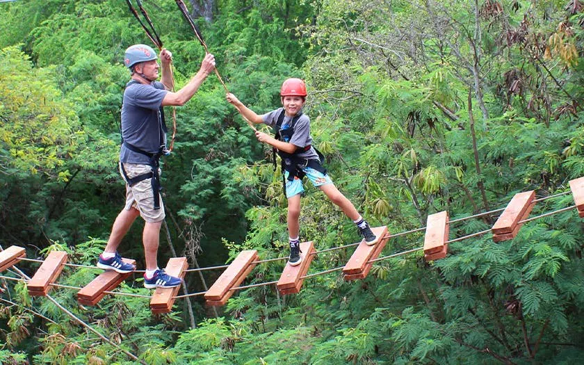Participants navigating a suspended wooden bridge on an adventure course in a forest setting.
