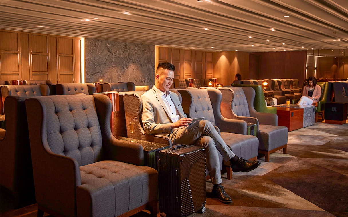 Man relaxing in a lounge chair with luggage at Hong Kong International Airport's first-class lounge.