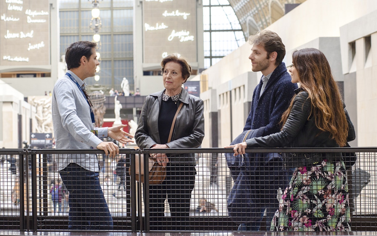 Guide with tourists inside Orsay Museum, France, discussing art exhibits.
