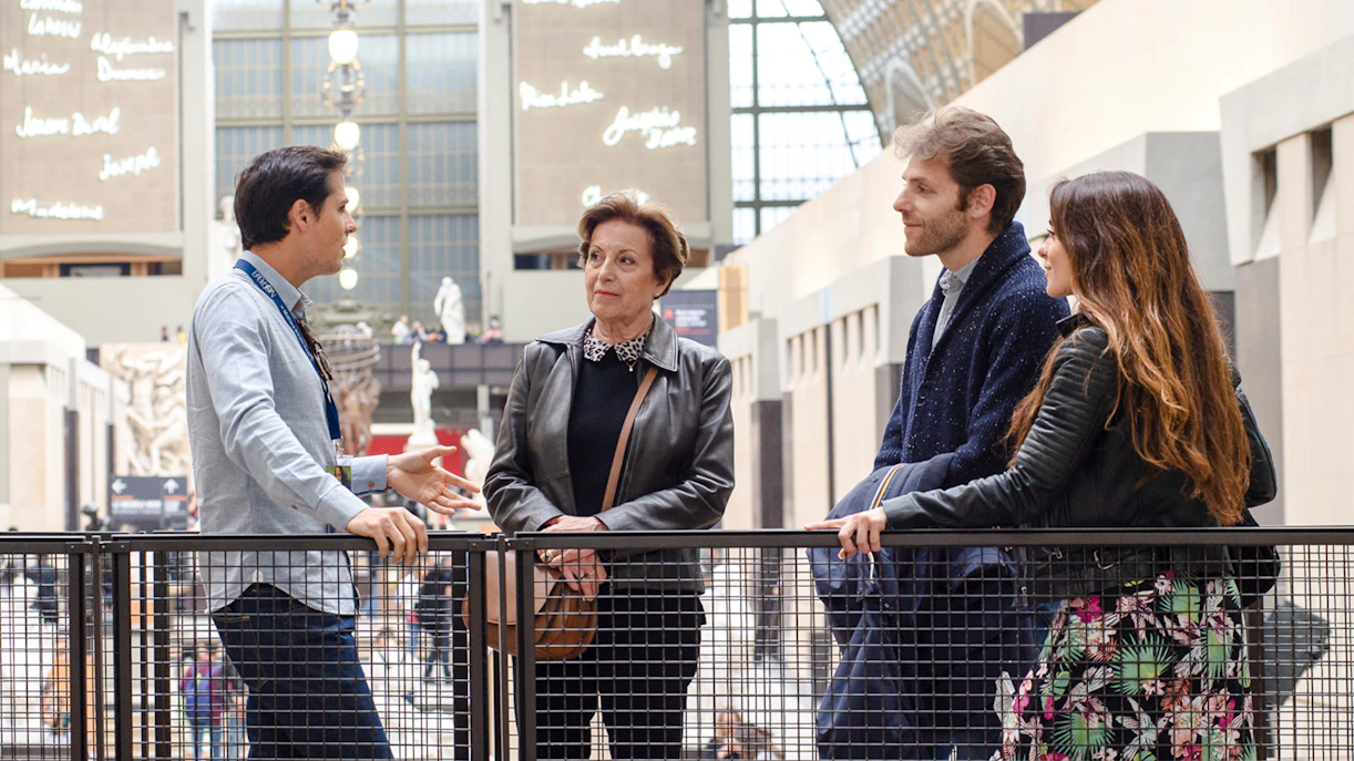 Guide with tourists inside Orsay Museum, France, discussing art exhibits.